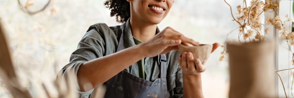 Young black ceramist woman wearing apron sculpting in clay at her workshop